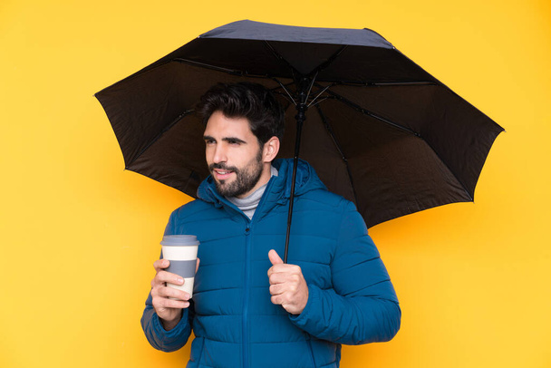 Чоловік тримає парасольку над ізольованим жовтим тлом
 - Фото, зображення