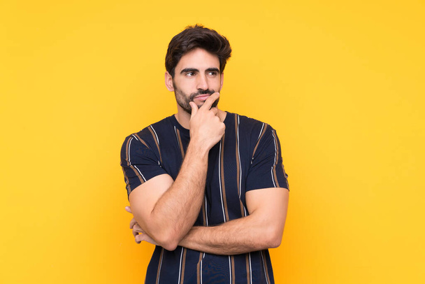 Junger gutaussehender Mann mit Bart vor isoliertem gelben Hintergrund denkt eine Idee nach - Foto, Bild