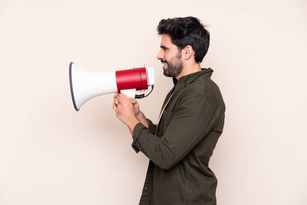 Young handsome man with beard over isolated background shouting through a megaphone - Photo, Image
