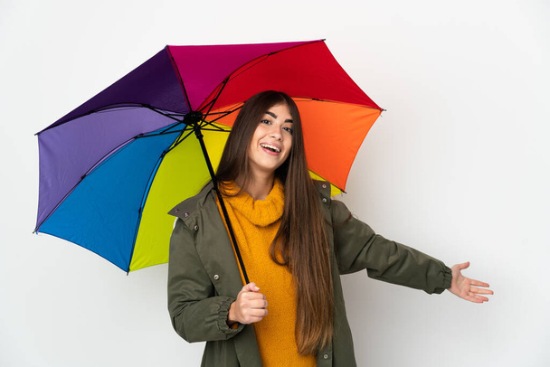 Mladá žena drží deštník izolovaný na bílém pozadí natahuje ruce na stranu pro pozvání přijít - Fotografie, Obrázek