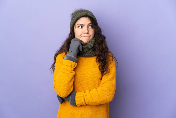 Неповнолітня російська дівчина з зимовим капелюхом ізольована на пурпуровому фоні має сумніви і мислення. - Фото, зображення