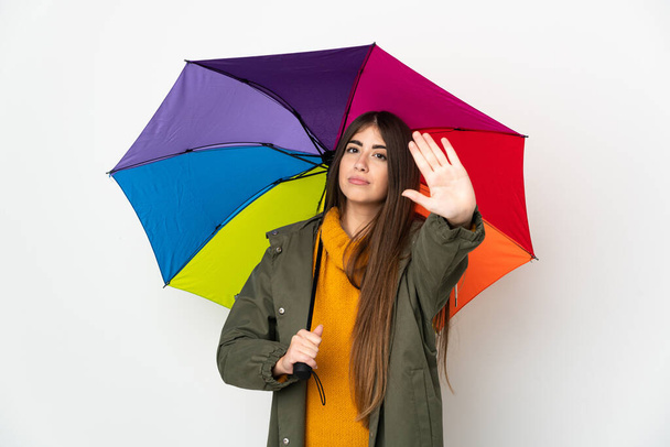 Young woman holding an umbrella isolated on white background making stop gesture - Photo, Image
