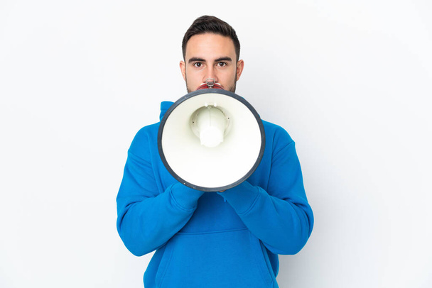 Young caucasian handsome man isolated on white background shouting through a megaphone to announce something - Фото, изображение