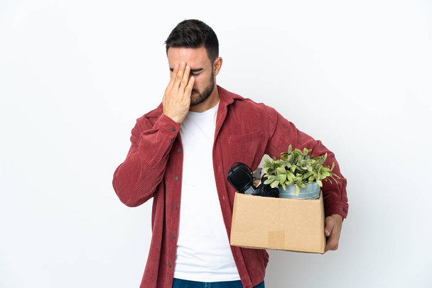 Νεαρός καυκάσιος άντρας κάνει μια κίνηση ενώ μαζεύει ένα κουτί γεμάτο πράγματα απομονωμένα σε λευκό φόντο με κουρασμένη και άρρωστη έκφραση - Φωτογραφία, εικόνα