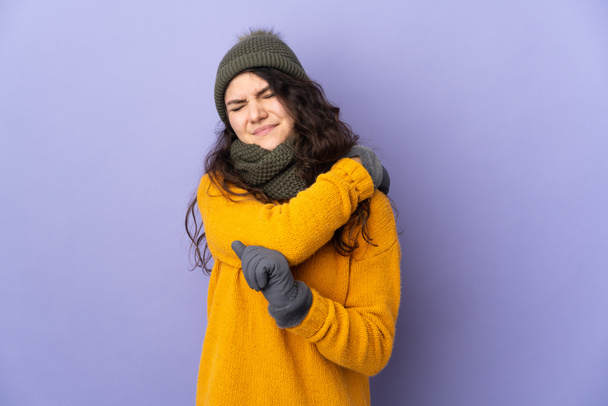 Teenager Russian girl with winter hat isolated on purple background suffering from pain in shoulder for having made an effort - Photo, Image
