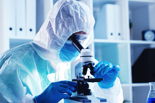 Medical worker in protective gown looking in microscope - Foto, Imagem