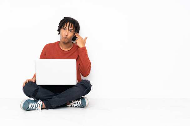 Mladý africký Američan sedí na podlaze a pracuje se svým notebookem s problémy dělat sebevražedné gesto - Fotografie, Obrázek