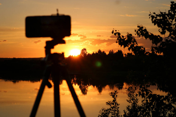 川の向こうにカラフルな夕日のスマートフォンでタイムラプス動画を撮影。選択的焦点. - 写真・画像