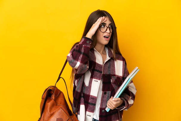 Young student woman isolated on yellow background doing surprise gesture while looking to the side - Foto, Imagen