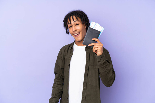 Young african american man isolated on purple background happy in vacation with passport and plane tickets - Zdjęcie, obraz