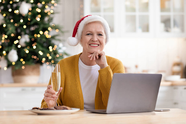 Belle mamie en chapeau de Père Noël assis devant un ordinateur portable - Photo, image