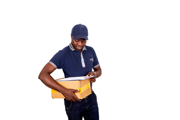 happy handsome young delivery man in blue uniform holding a paper press with empty paper document, and a cardboard looking at the camera - Photo, Image