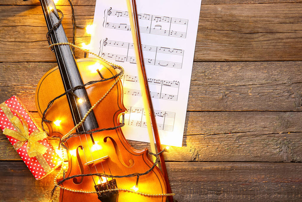 Violin with Christmas lights and music notes on wooden background - Φωτογραφία, εικόνα