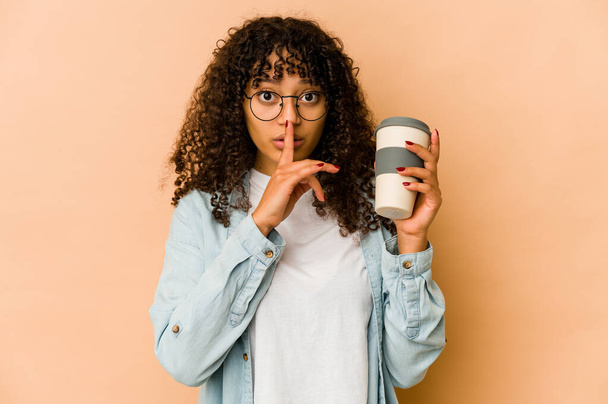 Νεαρή Αφρικάνα Αφρο-Αμερικανίδα που κρατάει καφέ για πακέτο κρατώντας μυστικό ή ζητώντας σιωπή. - Φωτογραφία, εικόνα