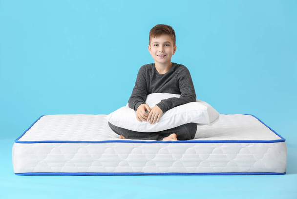 Roztomilý malý chlapec sedí na matraci proti barvě pozadí - Fotografie, Obrázek