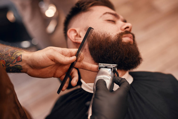 Crop barber trimming beard of dandy client - 写真・画像