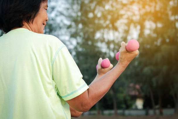 高齢者の女性はアジア人庭で健康のために運動するピンクのダンベルを上げる. - 写真・画像