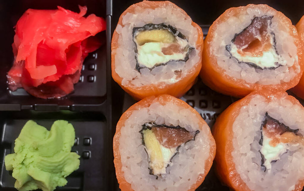 Japanisches Essen zum Mitnehmen - Reisbrötchen mit Lachs, Avocado und Frischkäse. Wasabi und roter Ingwer. Hintergrund der Nahrungsmittel. - Foto, Bild