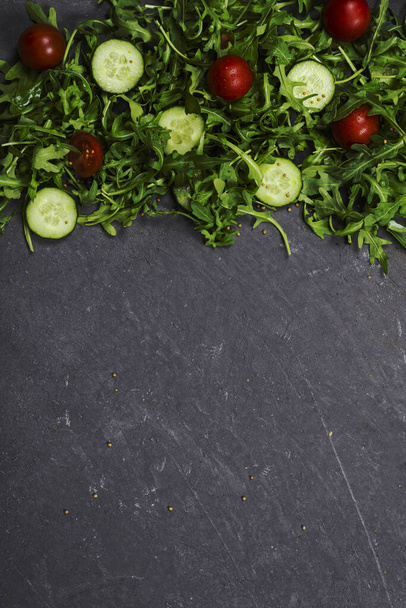 Fresh vegetables arugula, tomato, cucumber, herbs, peppercorns and olives on a vertical dark gray textured background. View from above. Place for text, copy space. - Фото, изображение