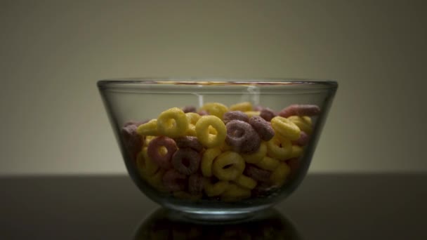 Gezond ontbijt met kleurrijke graanringen. Voorraadbeelden. Close-up van glazen transparante schaal met heerlijke zoete maïs ringen geserveerd op donkere tafel. - Video