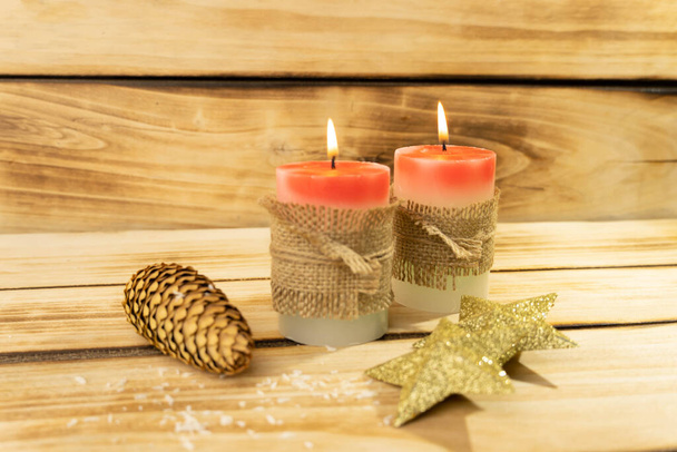 Christmas candles on a wooden background, shallow depth of field. Two red candles are wrapped in a sack rope, next to a shining Christmas star and a fir cone. Christmas background - 写真・画像