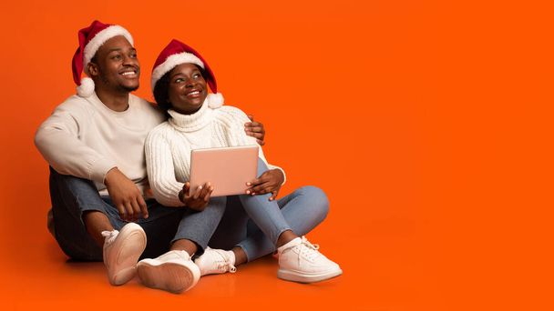 Zwarte echtgenoten in Santa hoeden houden digitale tablet, op zoek naar kopieerruimte - Foto, afbeelding