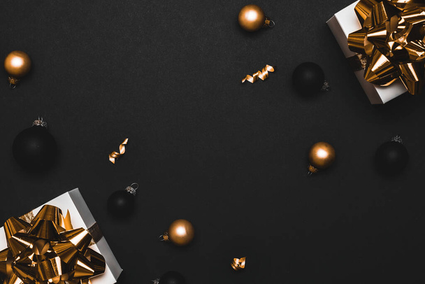 Weihnachtsdekoration. Weißes Geschenk mit goldener Schleife, goldenen Kugeln und funkelnden Lichtergirlanden in Weihnachtsdekoration auf dunklem Hintergrund zur Grußkarte. Flache Lage, Draufsicht, Kopierraum - Foto, Bild
