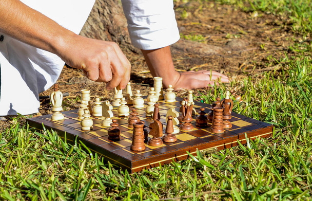 Egy közeli kép egy sakkozó emberről, aki a püspököt a sakktáblán mozgatja a kertben, a természetben. - Fotó, kép