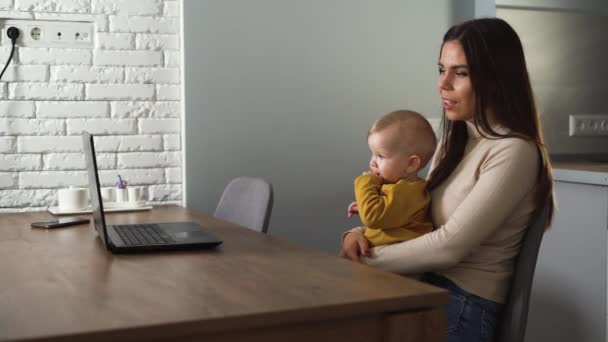 mamá y su hijo están sentados en casa en una computadora portátil y se comunican a través de la comunicación por video. Concepto de videollamada para seres queridos. - Metraje, vídeo