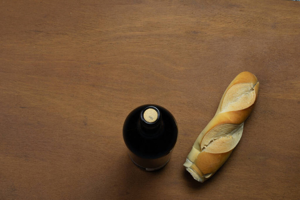 Botella de vino tinto y trozo de pan pelado en una mesa de madera - Foto, Imagen