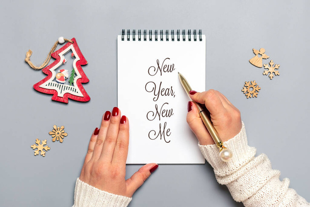 Жіноча рука тримає ручку і пише Новий рік, Новий Я на білому блокноті, дерево, сніжинку на сірому фоні Топ-вид Політ Бізнес мотивація, ідея, успіх, бачення, натхнення, план концепції. - Фото, зображення