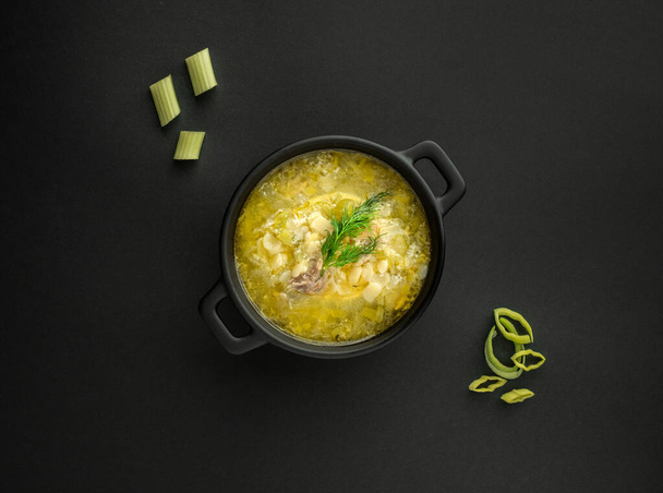 Avgolemono, traditional greek chicken soup with egg lemon sauce and dill in black pot on black background. Overhead shot with copy space. - Photo, Image