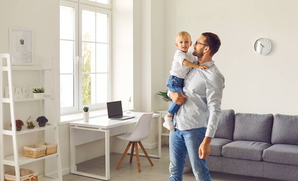 Young dad holding his happy little son standing in cozy room of their new apartment - Фото, изображение