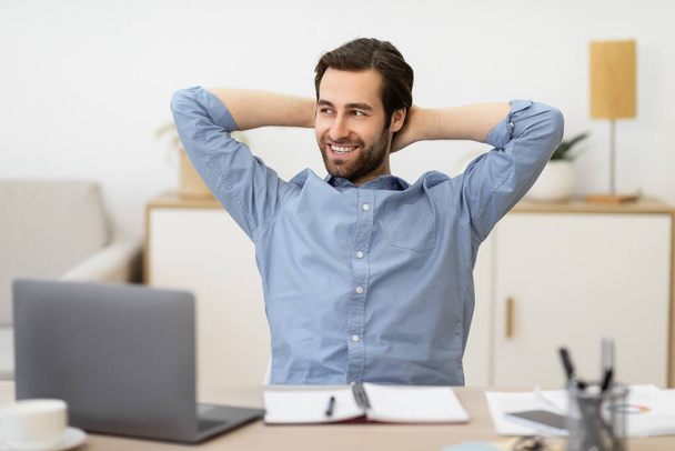 Безтурботний бізнесмен розслабляється сидячи тримаючи руки за головою на робочому місці
 - Фото, зображення