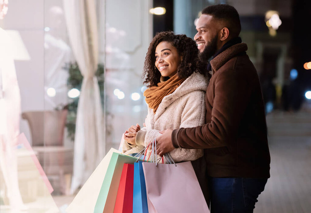 Feliz pareja afro con bolsas de compras mirando a la ventana del centro comercial - Foto, imagen