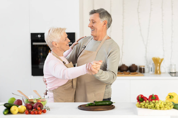 Idős házastársak táncolnak otthon a modern konyhában hétvégenként - Fotó, kép