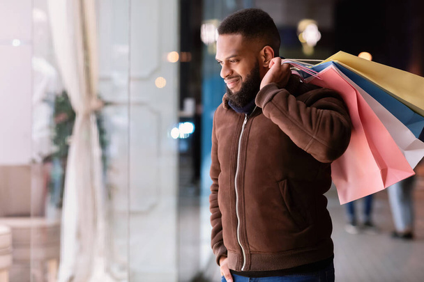 czarny facet z zakupy torby patrząc w centrum handlowym okno - Zdjęcie, obraz