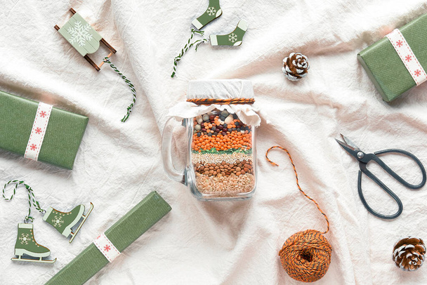 Zero waste Christmas gift in a jar. Layered bean mixture with spices on soft white textile background with no plastic wooden winter Xmas decorations and gifts wrapped in craft paper.. - Fotografie, Obrázek