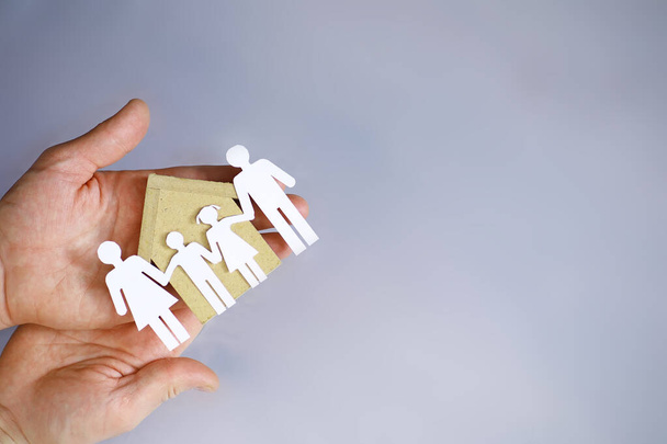 Cutout paper chain family with the protection of cupped hands, concept for security and care. Hands with cut out paper silhouette on table. Family care concept - Photo, Image