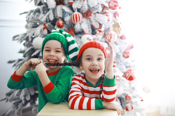 Los niños lindos en trajes de elfo de Navidad en una habitación bellamente decorada para la Navidad. Tiempo de milagros. Regalos de Santa Claus - Foto, imagen