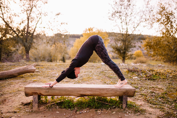 Vrouw die yoga beoefent en zich uitstrekt op de parkbank - Foto, afbeelding