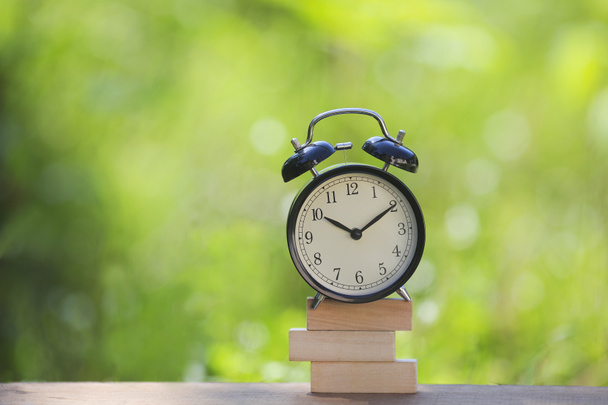 Relógio de alarme preto empilhado em barra de madeira com fundo verde raso DOF. Conceito de Gestão de Negócios / Tempo - Foto, Imagem