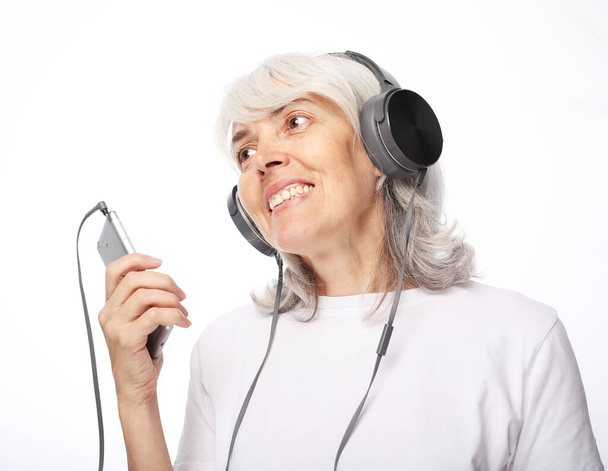 Elderly woman listens to music on headphones over white background - Zdjęcie, obraz