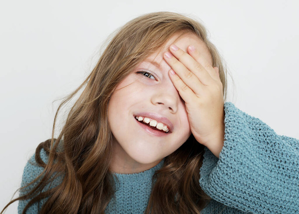 Adorable little girl with long curly blond hair closes her eyes with her palm - Foto, afbeelding