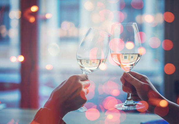 Two hands with glasses with white wine on the background of a window close-up, celebrating the holidays - Photo, Image