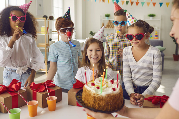 Group of happy diverse kids celebrating their friends birthday at fun party at home - Фото, изображение