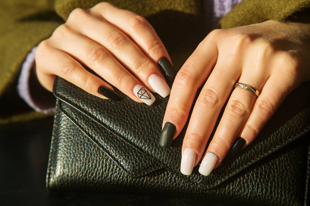 mãos de mulheres com uma bela manicura em uma carteira de couro preto, foto ensolarada.  - Foto, Imagem