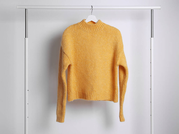 Warm sweater hanging on rack against white background - Foto, imagen