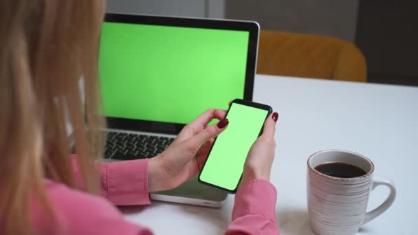 Close up Frau mit Smartphone grünen Bildschirm auf dem Tisch mit Laptop-Computer Chromakey. Nahaufnahme von Frauenhänden, die ihr Mobiltelefon halten und den grünen Bildschirm scrollen.. - Filmmaterial, Video