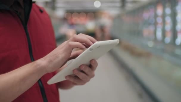 Filmato a sezione centrale di mani maschili irriconoscibili di merchandizer ipermercato che digita su tablet bianco prendendo appunti sulle vendite - Filmati, video